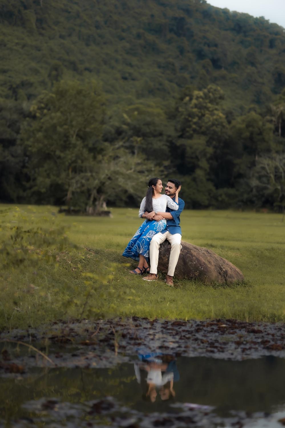 Joji and Bismi sitting on a rock by the water, reflected below